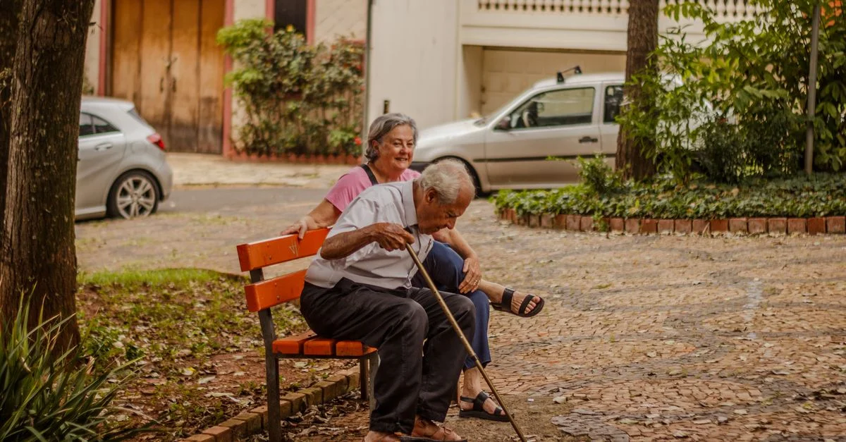 Un couple senior profitant d'un moment paisible sur un banc de parc dans un environnement urbain avec des voitures et de la verdure.
