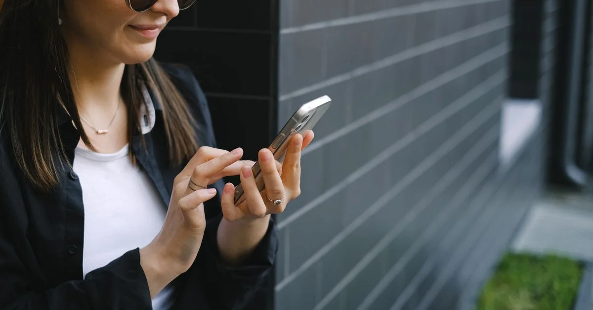 Une jeune femme confiante utilise un smartphone à l'extérieur près d'une façade de bâtiment moderne.