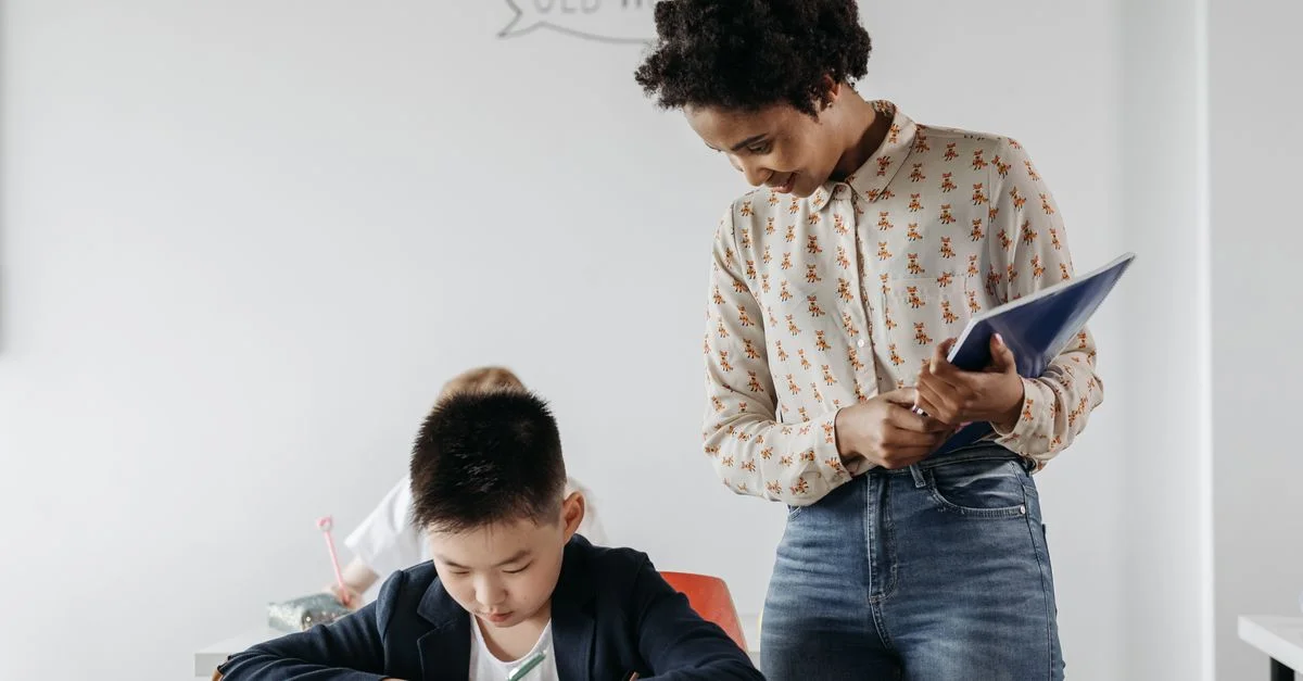 Un enseignant guide un élève dans une salle de classe, favorisant un environnement d'apprentissage et de soutien.