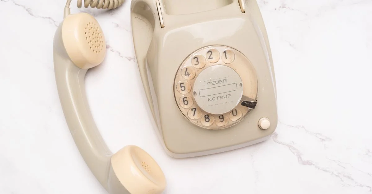 Téléphone rotatif beige classique sur marbre, évoquant la nostalgie et l'élégance.