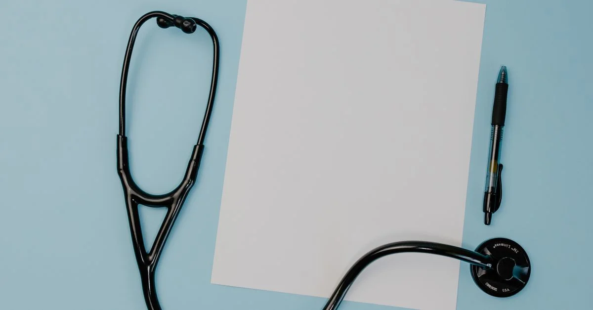 Vue de dessus d'un stéthoscope, papier vierge et stylo sur un fond bleu.