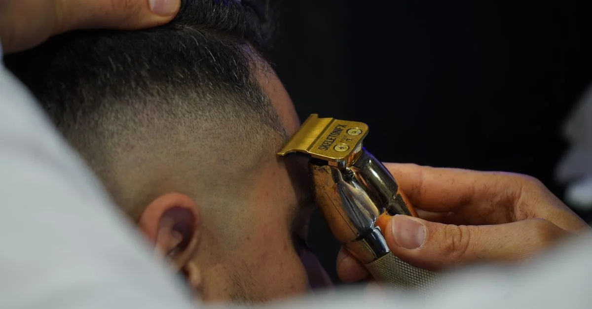 Gros plan d'un barbier utilisant un rasoir électrique pour un toilettage précis sur la tempe d'un client.