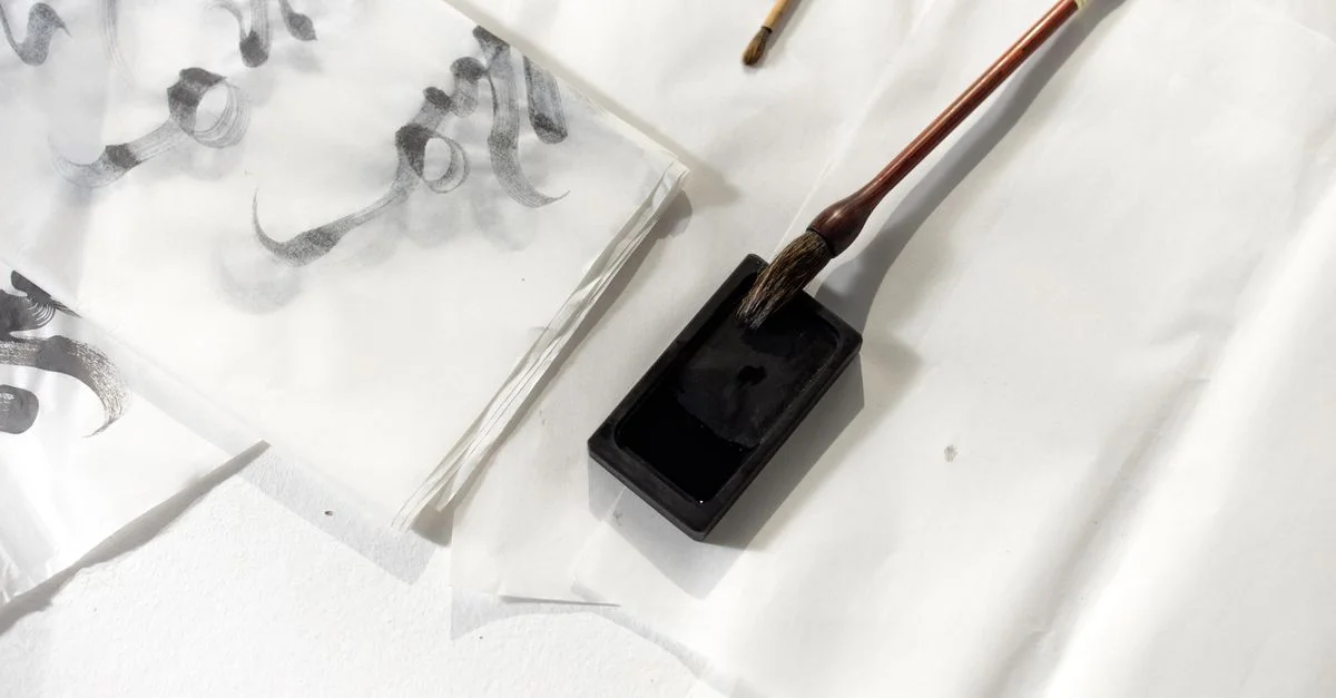 Gros plan sur des outils de calligraphie et de l'encre sur du papier, mettant en évidence les techniques artistiques traditionnelles.